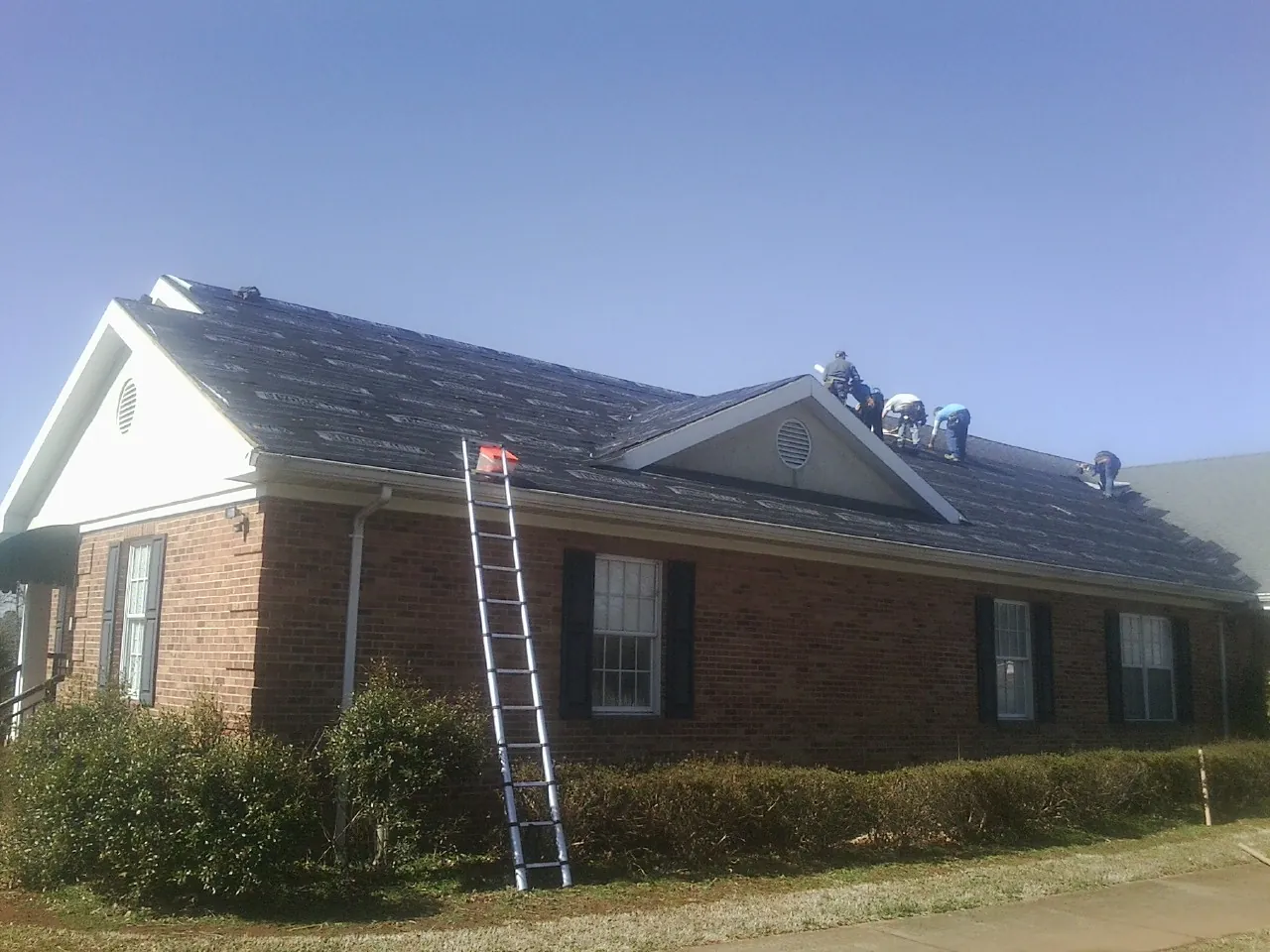 Crew tearing shingles off a brick ranch roof with a ladder set — Metal Roof Repair work by our crew in Kenilworth