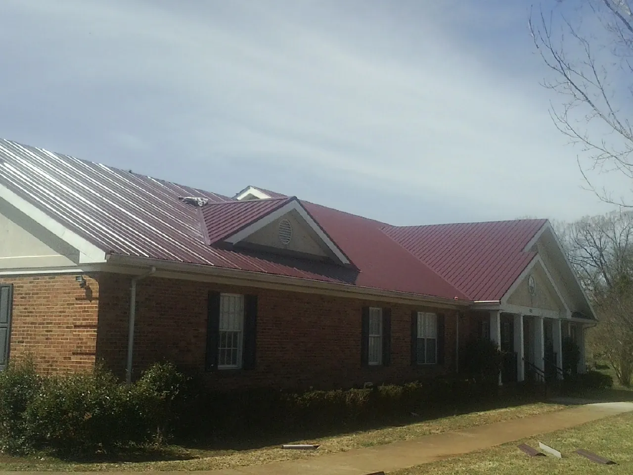Red metal roof with gabled entries on a long brick building, from a Hail Damage Roof Repair job in Kenilworth