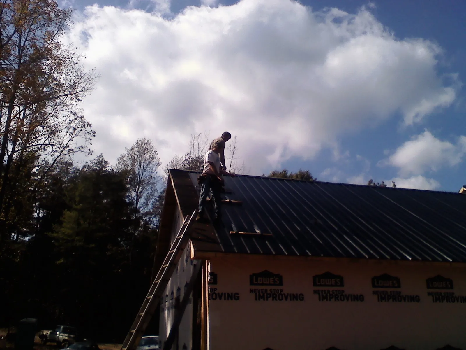 Roofer fastening dark metal panels high against a cloudy sky, from a Roof Inspection job in Kenilworth
