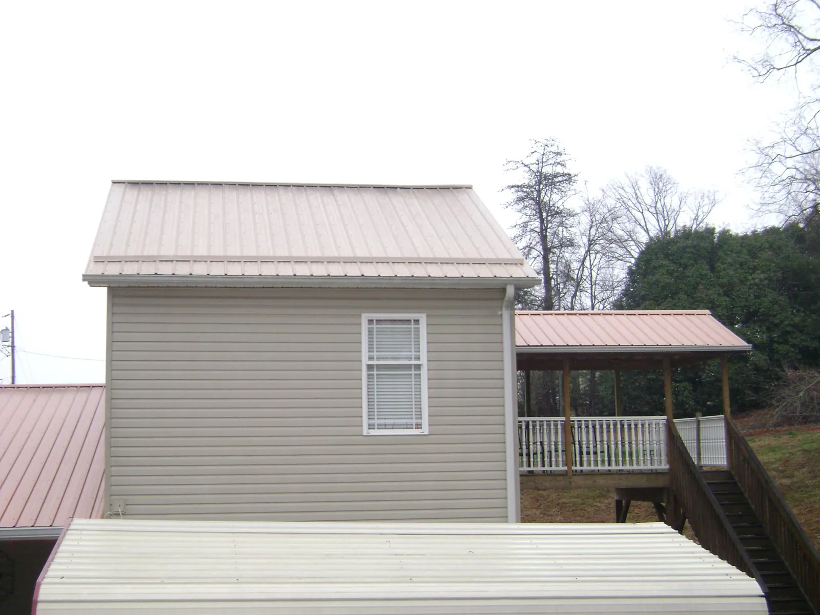 Tan metal roofs on a two story addition and attached porch, from a Roof Replacement job in Kenilworth